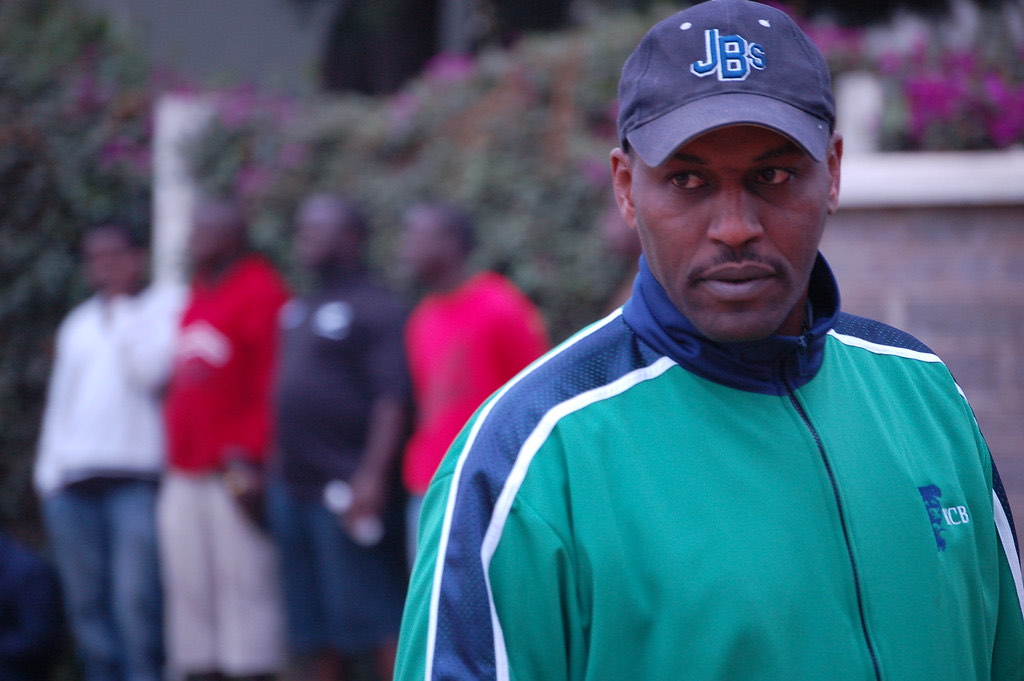 A coach in a tracksuit and cap watching his side train