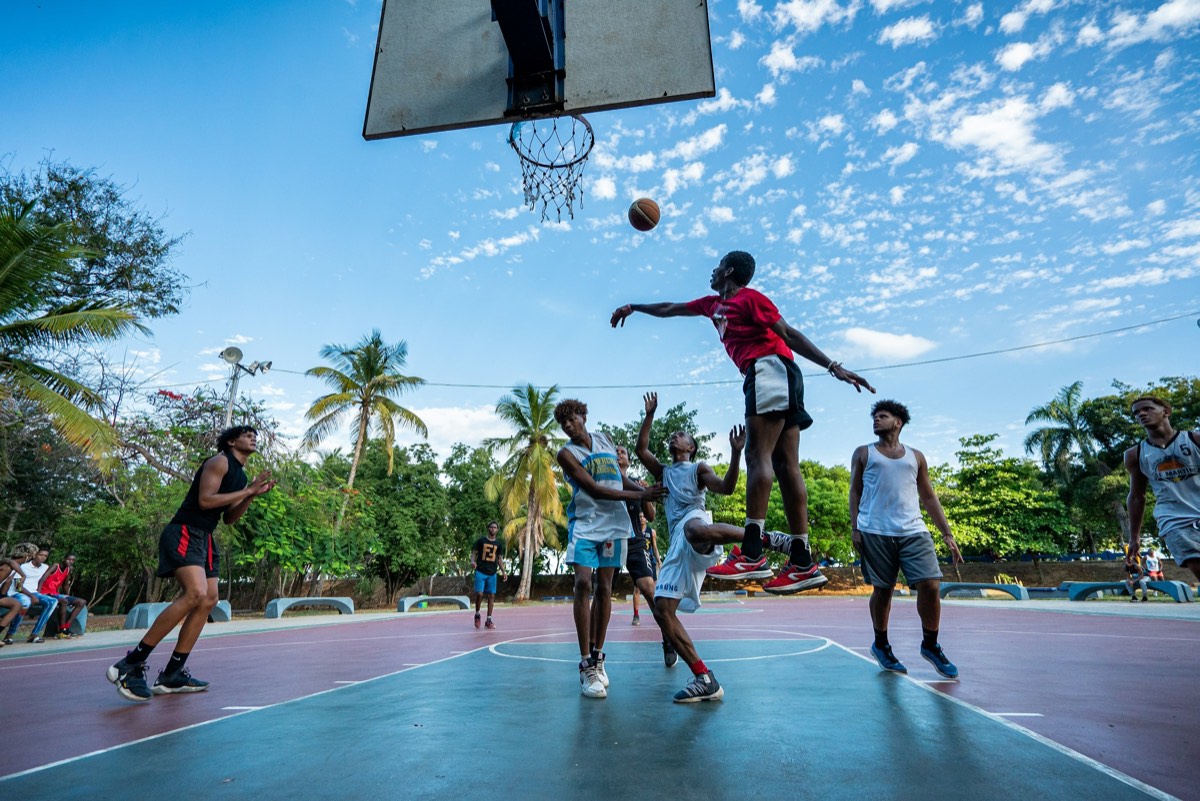 A player rising to the basket on an outdoor court, the ball in the air