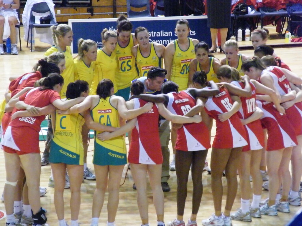 Two netball teams in their own huddles at the side of an indoor court