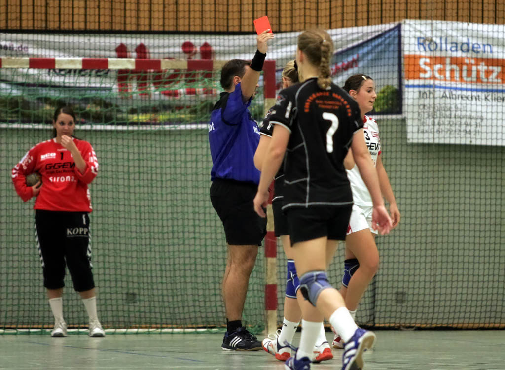 A referee holding a red card above their head towards a player