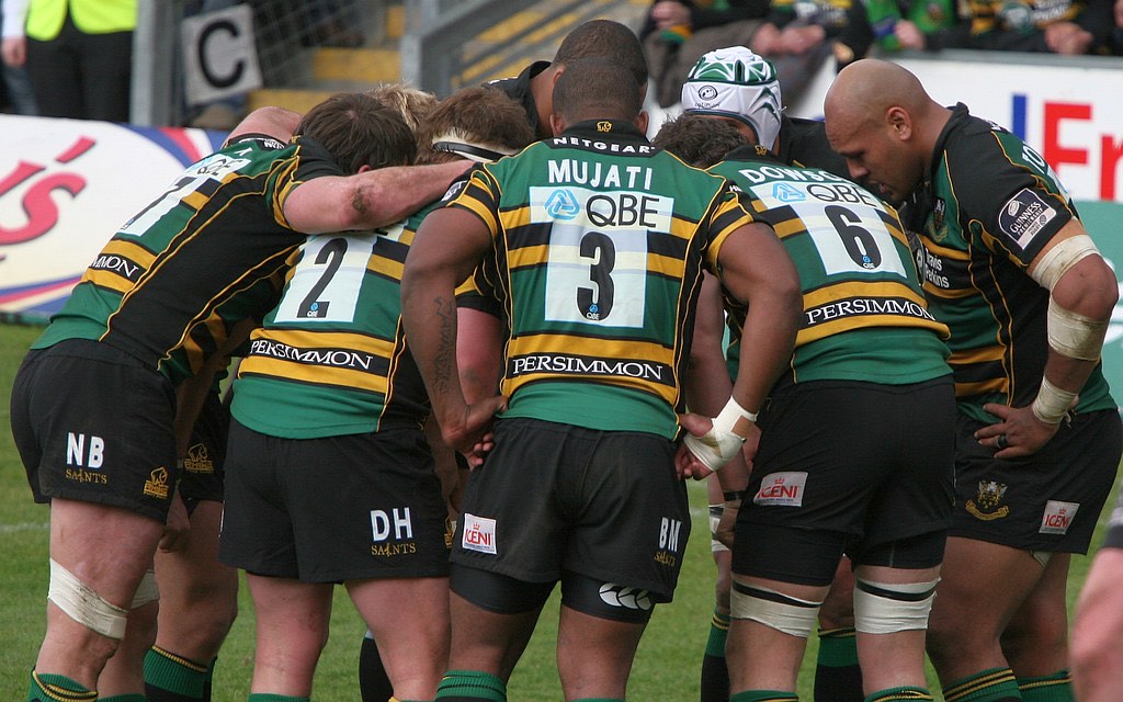 A rugby team in a huddle, squad numbers across their backs