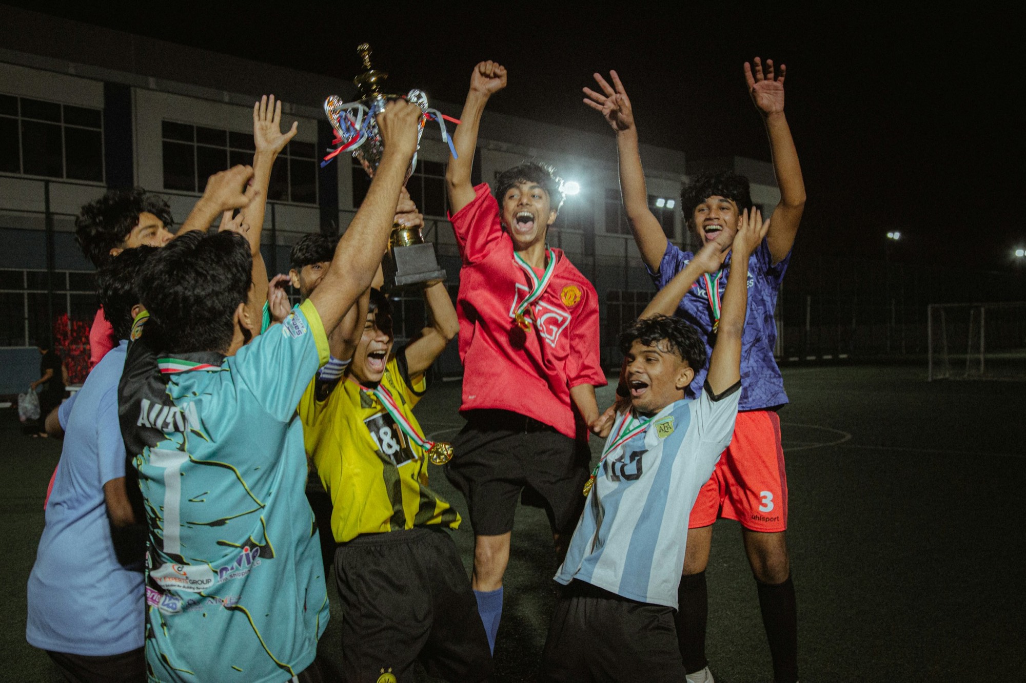 A side celebrating under the floodlights with the trophy above their heads