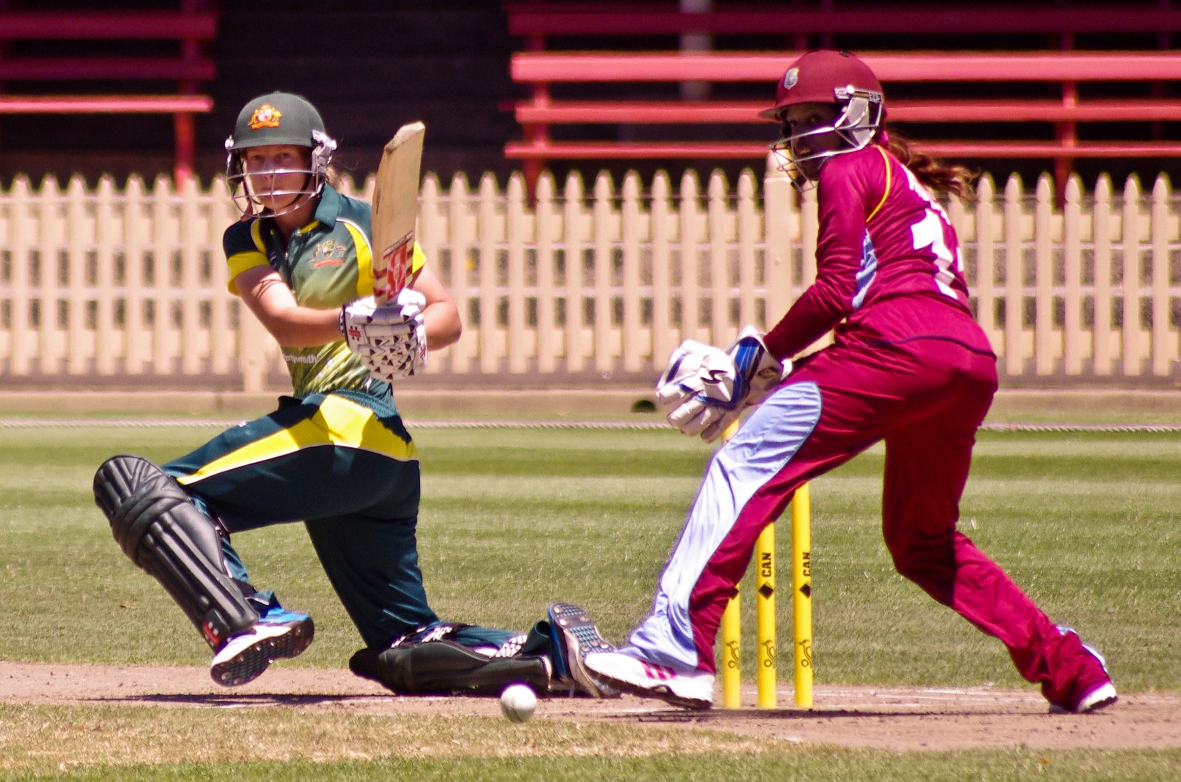 A batter sweeping and a wicketkeeper crouched behind the stumps in a women’s cricket match